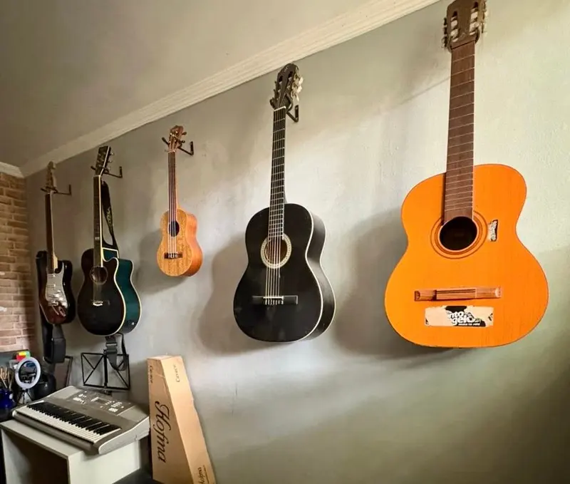 Instrumentos de corda pendurados na parede, entre eles guitarra e violões, com um teclado no canto